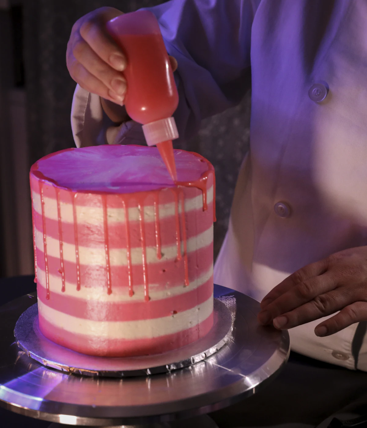 Baker piping pink frosting onto a layered cake