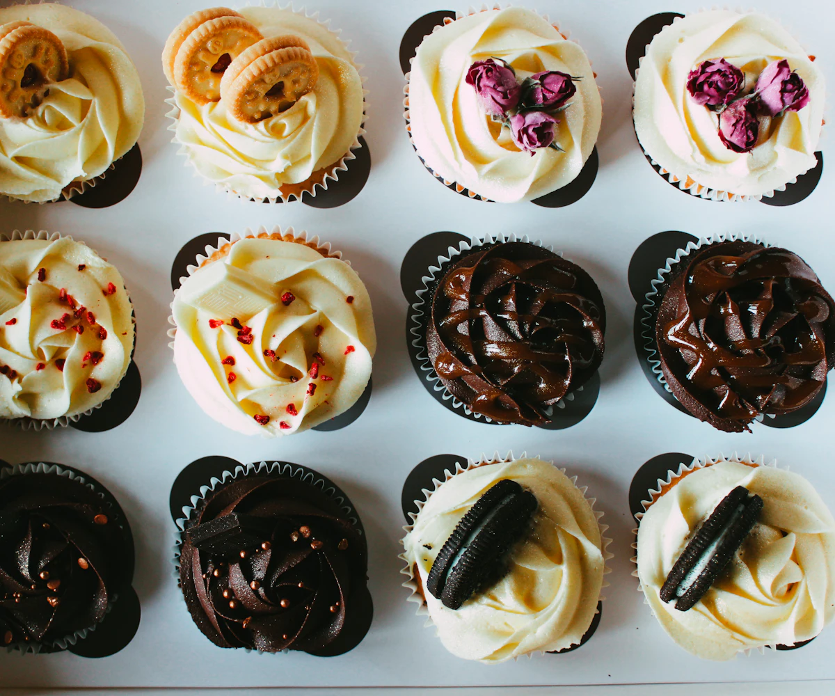 A dozen assorted cupcakes in an open bakery box