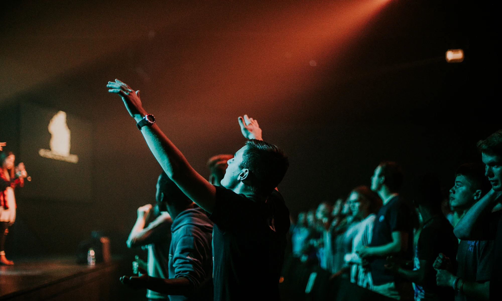 A congregation worshiping with hands raised under warm stage lights