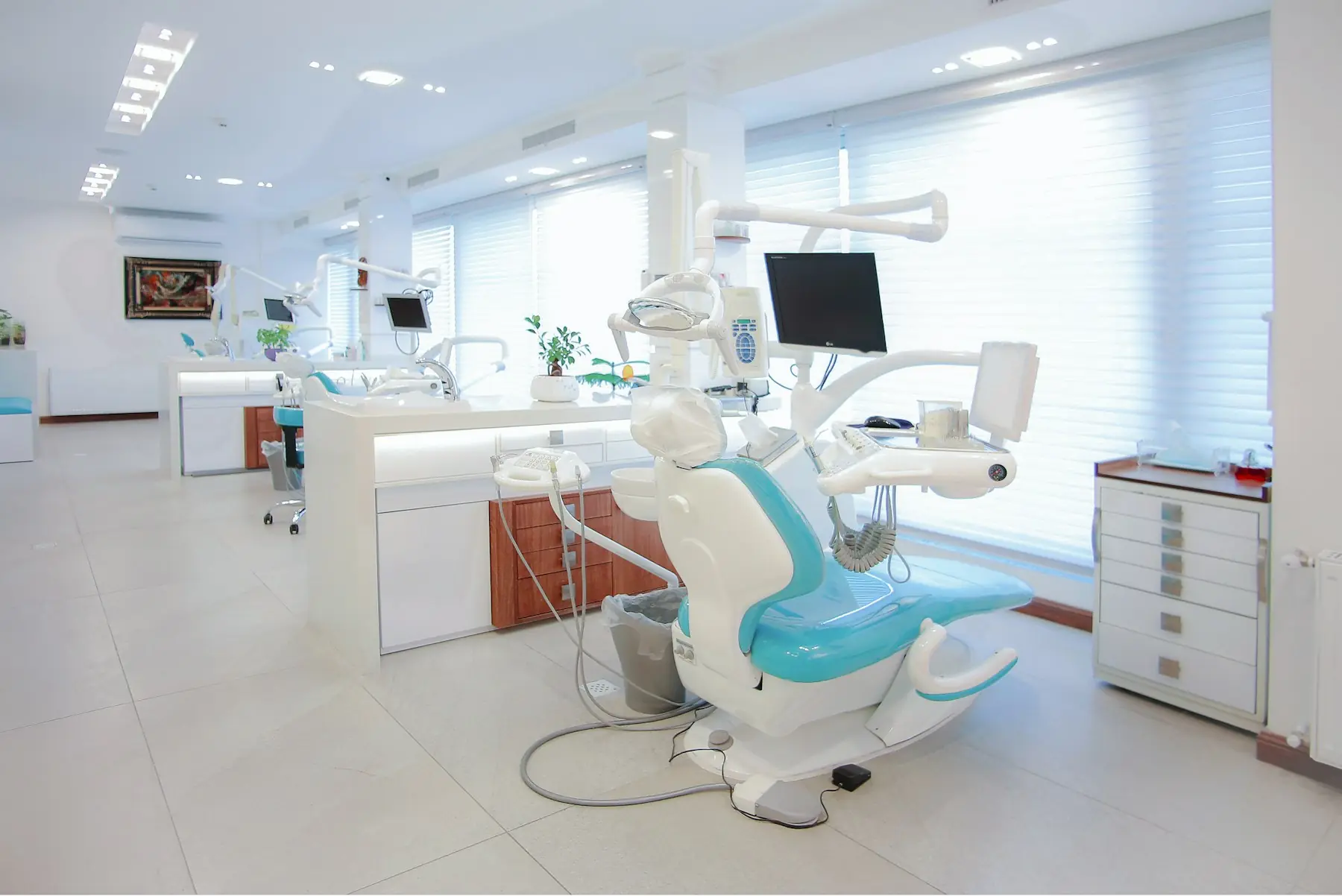 A bright treatment room at Maple & Main Dental with a teal chair and a wall of windows
