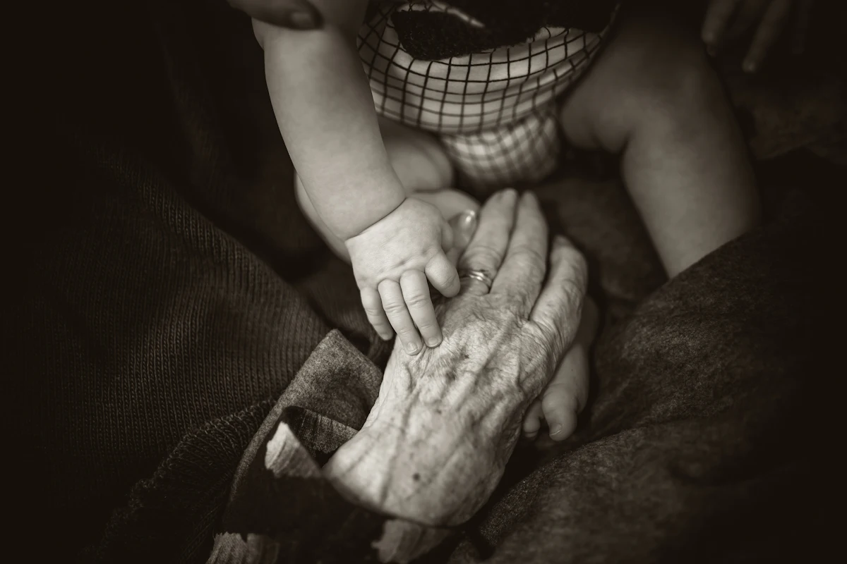 An elderly hand gently holding a baby's hand