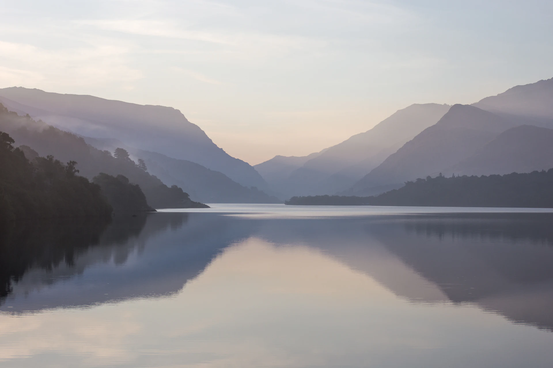 Still mountain lake at dawn under soft clouds