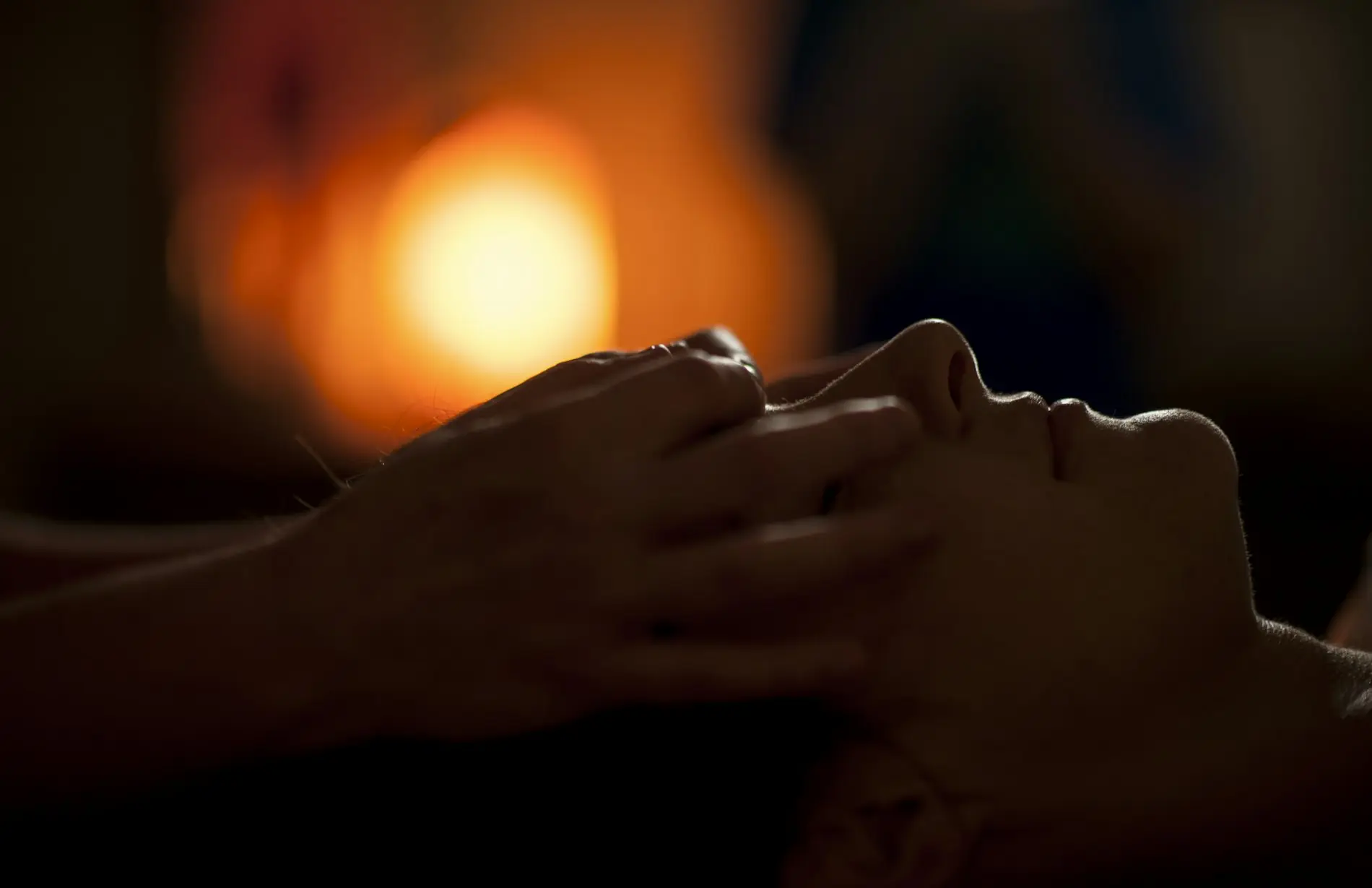A provider's hands resting on a client's face in warm, low light