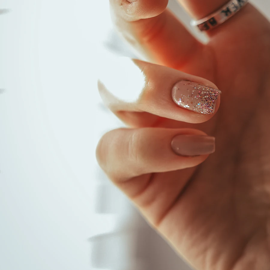 Nude nails with a glitter accent and gold ring