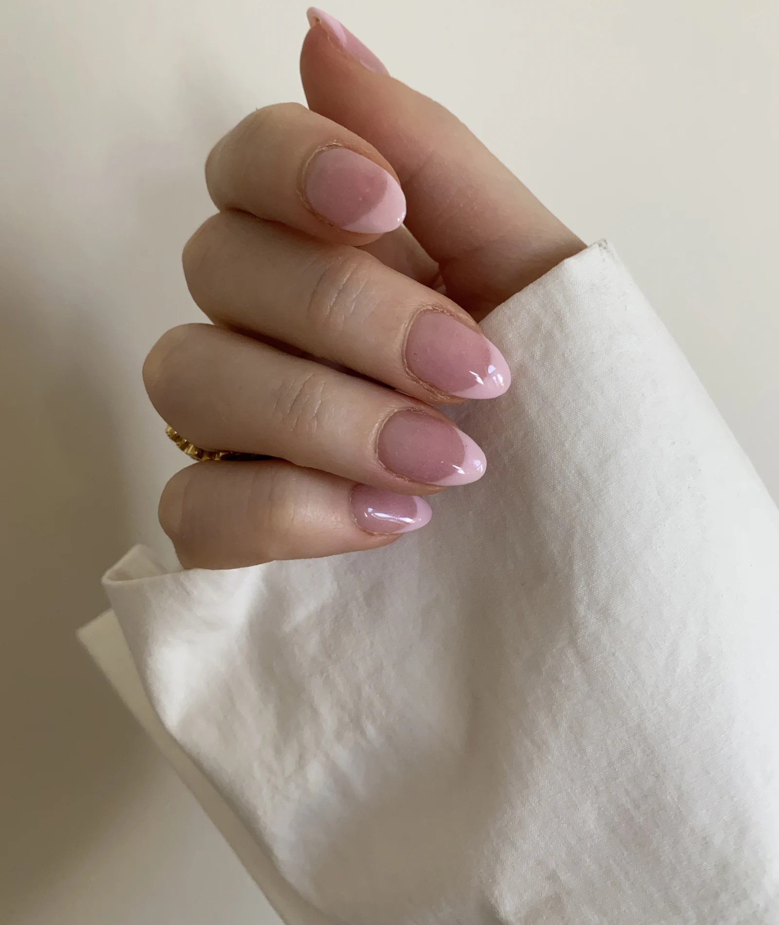 Elegant almond-shaped blush pink gel manicure resting on soft white fabric